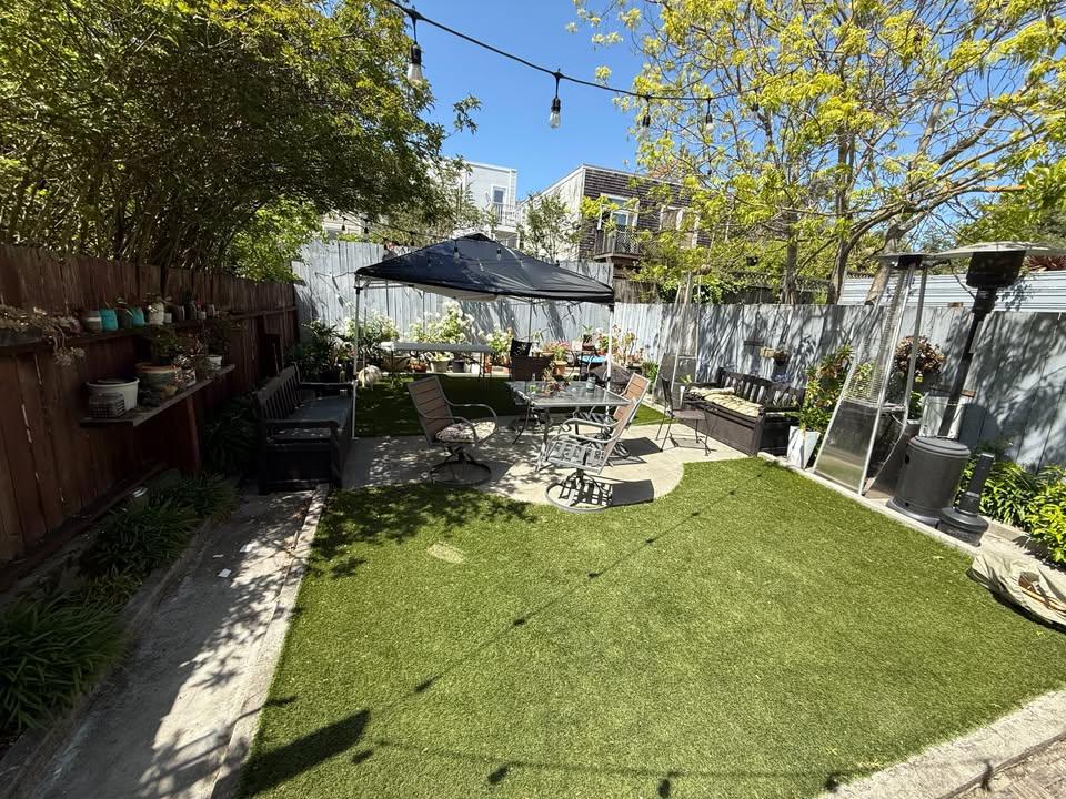 Sunny backyard with patio furniture, string lights, and green grass